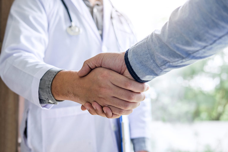 Professional Male doctor in white coat handshake with patient